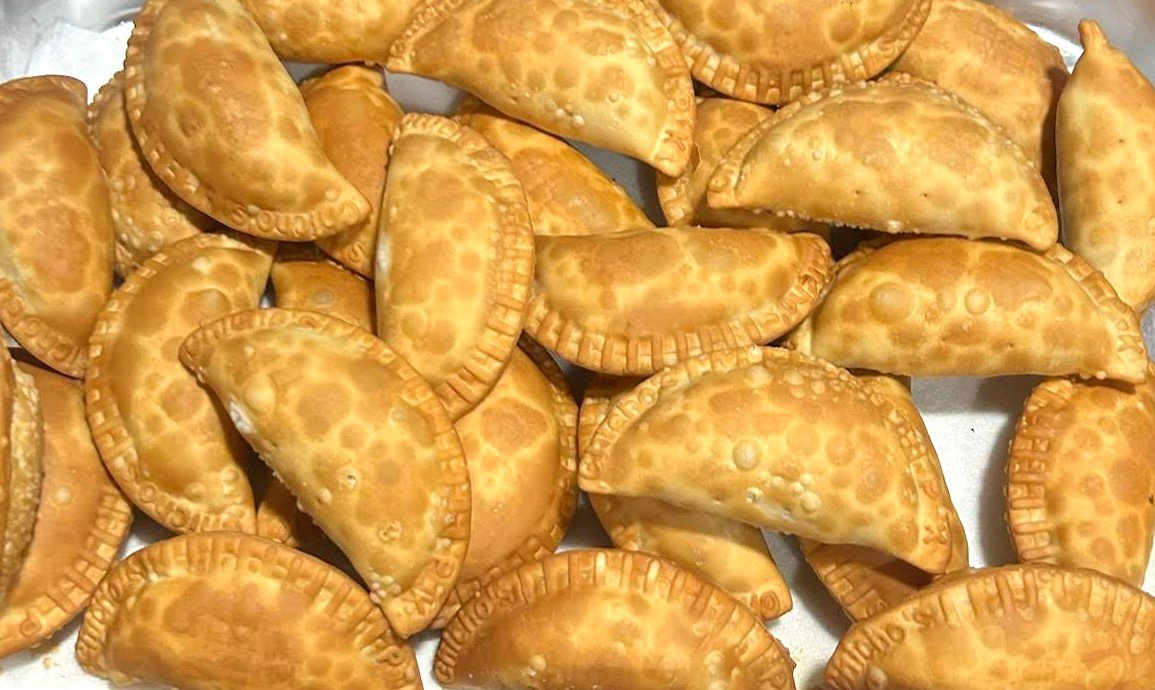 A tray of golden Dominican empanadas with Chicho's pressed into the crimped edges