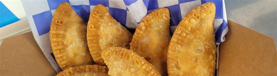 A box of savory empanadas on blue checkered paper, each crust pressed with the Chicho's name